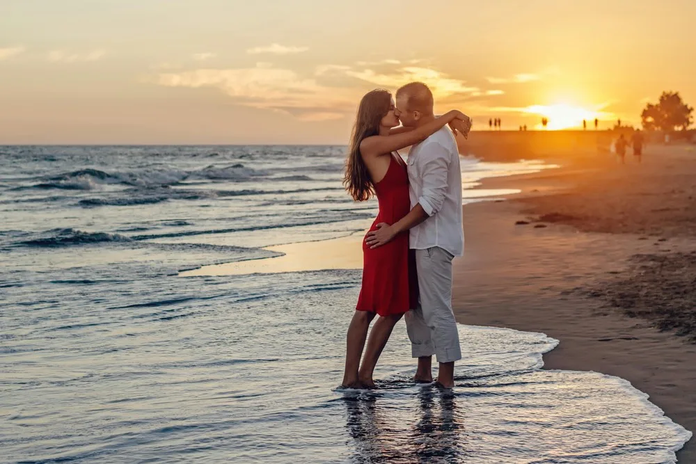 Un couple dans un moment de séduction au bord de la plage s'embrasse les pieds dans l'eau